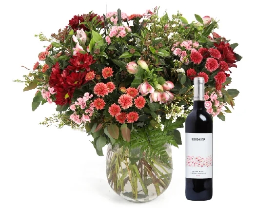 זר פרחים 'קסם המדבר' בגווני ורוד, בורדו, לבן וענפים ירוקים בשילוב בקבוק יין אדום