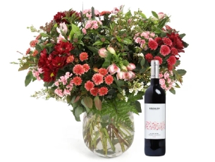 זר פרחים 'קסם המדבר' בגווני ורוד, בורדו, לבן וענפים ירוקים בשילוב בקבוק יין אדום