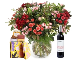 זר פרחים 'קסם המדבר' בגווני ורוד, בורדו, לבן וענפים ירוקים בשילוב בקבוק יין אדום ומארז שוקולד